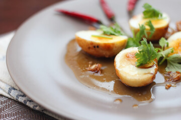 Egg with Tamarind Sauce in a white plate served on a wooden table with coriander sprinkles, is a popular local dish that Thai people eat.