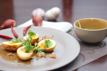 Egg with Tamarind Sauce in a white plate served on a wooden table with coriander sprinkles, is a popular local dish that Thai people eat.