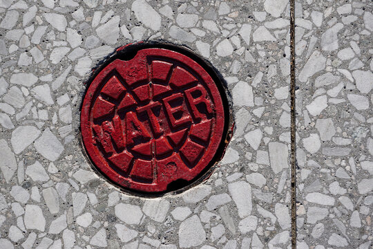 Round red metal cover on stone patterned city sidewalk, concept image for healthy drinking water, contamination issues.