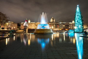 Christmas decorations and menorah in Trafalgar Square in London. Long exposure shot with blurred water and reflections: London, England- December 20,2021 - obrazy, fototapety, plakaty