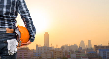 Back view of the business or engineering smart holding orange helmet  on a city background.
