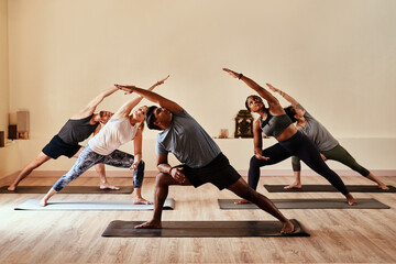 Yoga lets your inner warrior loose. Shot of a group of young men and women practicing yoga in a...