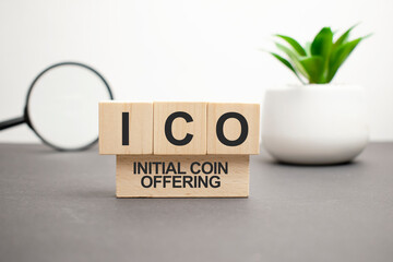 letters of the alphabet of ICO on wooden cubes, green plant on a white background. ICO - short for initial coin offering