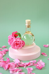Rose essential oil in a glass bottle in rose flowers on a pink podium on a green background.Aromatherapy and cosmetics. natural rose oil.Organic bio cosmetics 