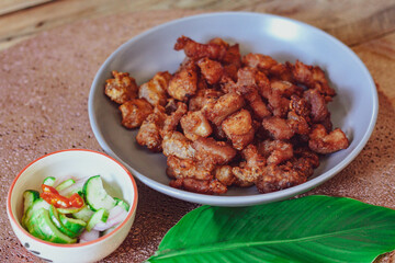 Fried Pork Belly with Fish Sauce and Sticky Rice Served on a white plate on a black wooden floor.