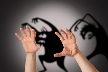 Hands of scared man and silhouettes of monsters on grey background. Concept of fear and nightmare