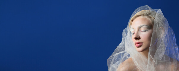 Beautiful young woman with creative makeup and veil on blue background with space for text
