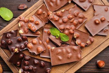Board with pieces of tasty chocolate and nuts on table