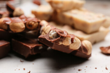 Pieces of tasty chocolate with hazelnuts on table, closeup