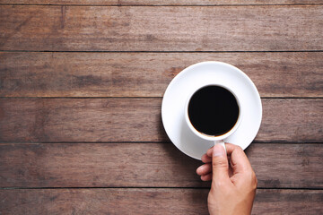 Male hand hold mug of coffee on wood table.