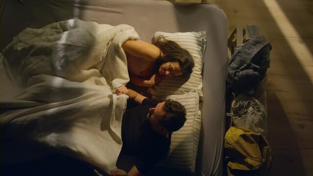 Overhead view of mid-adult couple lying in bed nad kissing at night