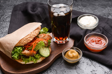 Fresh doner kebab in bun with sauces and glass of cola drink on dark background