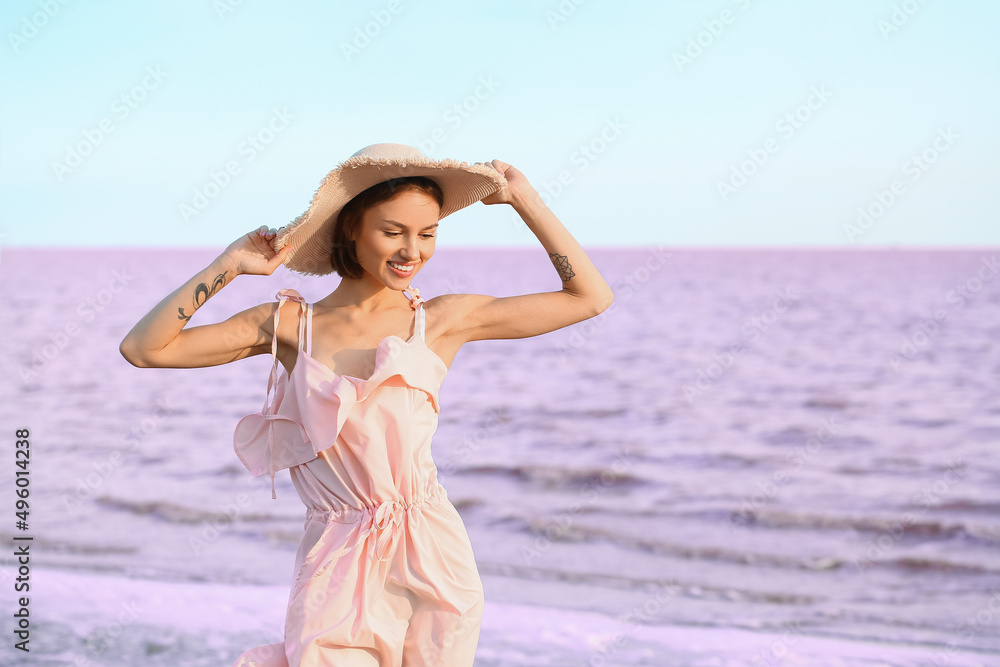 Poster Stylish young woman posing near pink lake on summer day