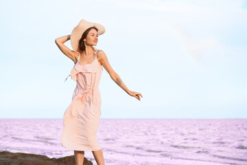 Fototapeta na wymiar Stylish young woman posing near pink lake on summer day