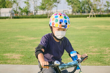 Cute little 5 years old toddler boy child in safety helmet wearing medical face mask riding a bike...