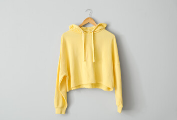 Stylish yellow hoodie hanging on light wall