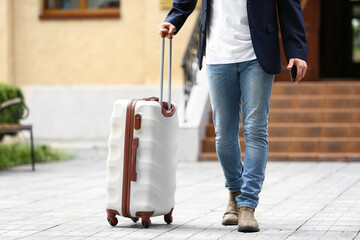 Young man with mobile phone and suitcase outdoors