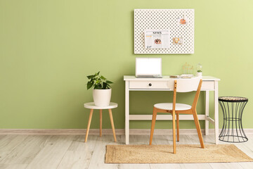 Modern workplace with different supplies and peg board on green wall