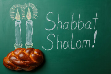 Drawn glowing candles and written text SHABBAT SHALOM with traditional challah bread on chalkboard
