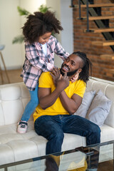 Girl standing on couch hugging her sitting dad