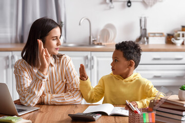 Little African-American boy with tutor raising hands at home