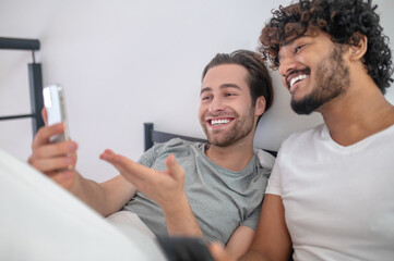 Joyful guy demonstrating photos on the cellphone to his companion