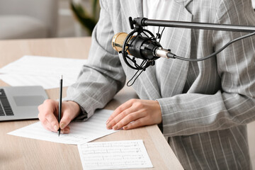 Woman writing on note sheet and modern microphone in room, closeup