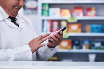 Always on the look out for new medical breakthroughs. Shot of an unrecognizable pharmacist using a cellphone in a pharmacy.