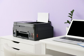 Workplace with modern laptop and chest of drawers with printer near color wall