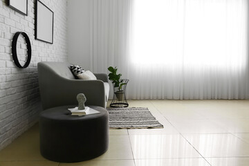 Pouf with stylish decor and sofa near white brick wall in light room