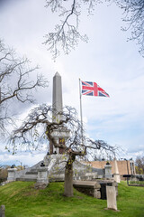 A tall gravestone is accompanied by a British flag, waving in the wind, in Drummond Hill Cemetery in Niagara Falls, Ontario.