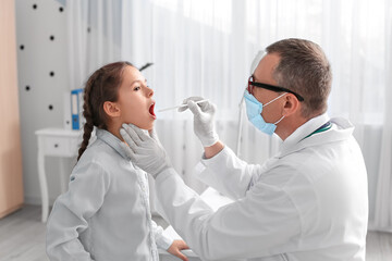 Doctor examining little girl with sore throat in clinic