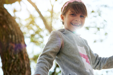 If I could I would play outside all day. Portrait of a little girl sitting in a tree in a park.