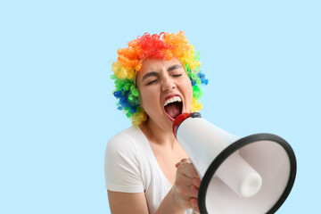 Funny young woman in colorful wig and with megaphone on blue background. April fools' day...