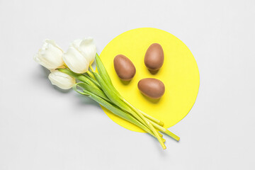 Delicious chocolate eggs and beautiful tulip flowers on light background