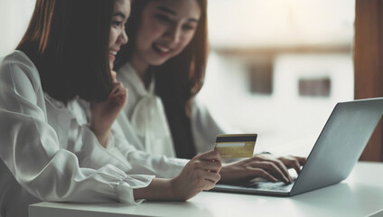 Two young asian women holding credit card and using laptop computer for shopping on line with happiness, business and technology concept, digital marketing, casual lifestyle