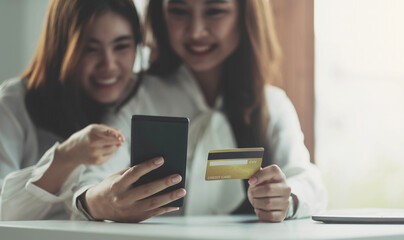 Two young Asian women hold credit cards and happily use their mobile phones for online shopping. business concept and technology digital marketing casual lifestyle