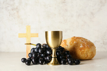 Cup of wine with grapes, bread and cross on light background