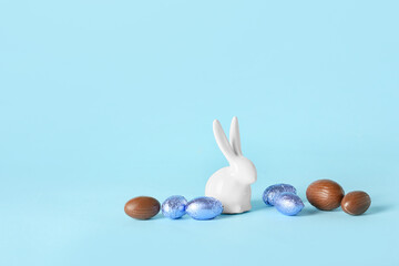 Chocolate Easter eggs and ceramic bunny on color background