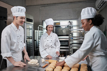 Professional gourmet team, three young chefs in white cook uniforms and aprons knead pastry dough...