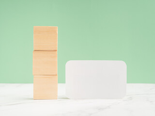 Three blank wooden cubes and a blank white paper on a marble floor against a light green background