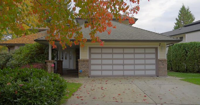Establishing shot of two story stucco luxury house with garage door, big tree and nice Fall Foliage landscape in Vancouver, Canada, North America. Day time on Sept 2021. ProRes 422 HQ.