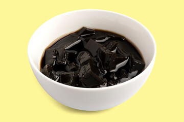 Grass jelly, gelatin or black jelly with sweet syrup, Chinese style dessert isolated on yellow background. Clipping path.
