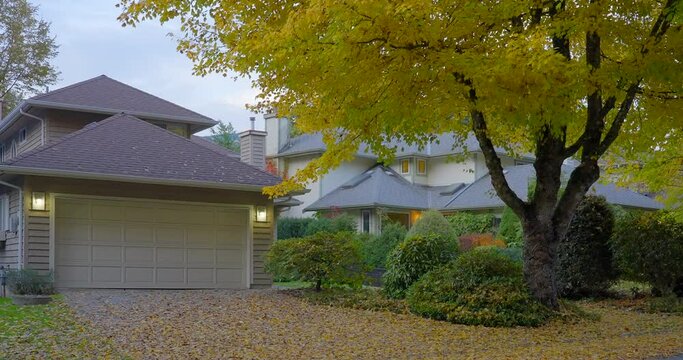 Establishing shot of two story stucco luxury house with garage door, big tree and nice Fall Foliage landscape in Vancouver, Canada, North America. Day time on Sept 2021. ProRes 422 HQ.