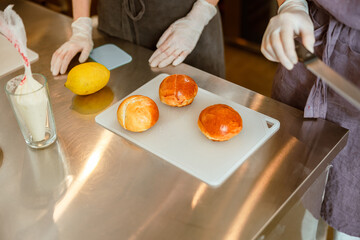 Confectioners with buns, cream and lemon at metal table in craft bakery