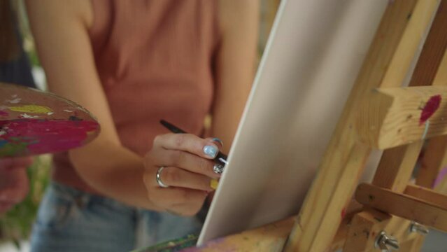 Two lovely girlfriends are standing in the studio, smiling and drawing a picture together