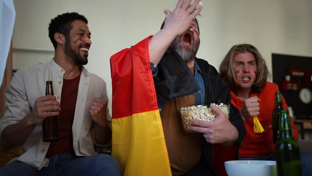 Happy German football fans friends watching football at home and applauding
