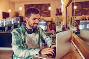 Cheerful bearded man working on laptop in cafeteria