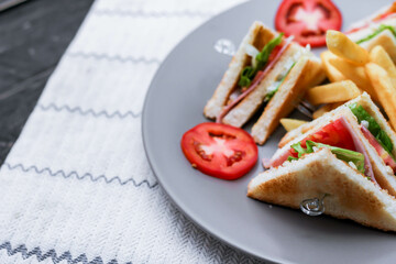 4 club sandwich slices laid out on a gray plate with tomatoes and fries.