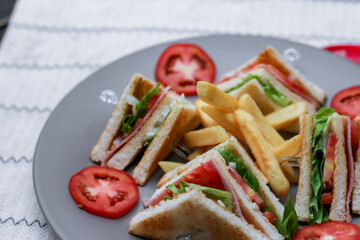 4 club sandwich slices laid out on a gray plate with tomatoes and fries.